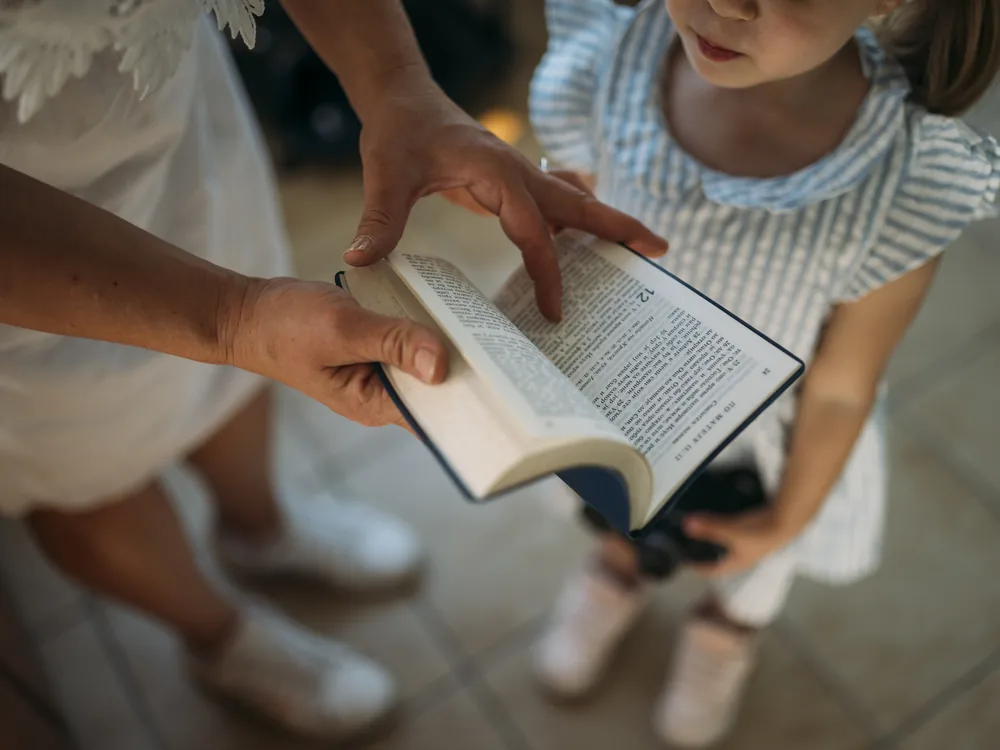 A child attentively following along as an adult reads from a book indoors